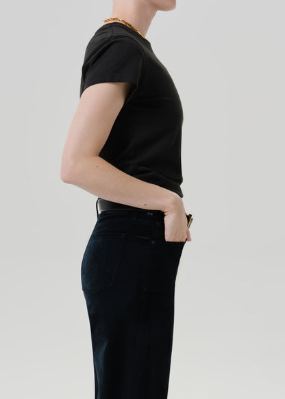 Person wearing a black short sleeve crewneck tee with black wide leg jeans viewed from the side on a grey background