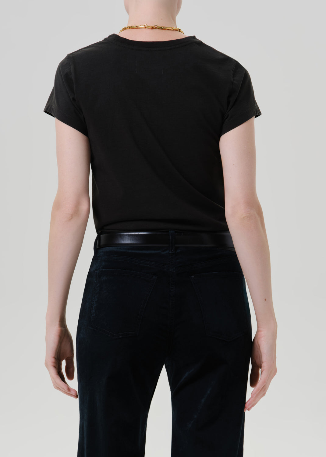 Person wearing a black short sleeve crewneck tee with black wide leg jeans viewed from the back on a grey background