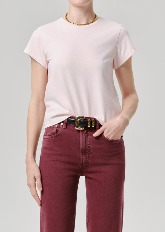 Person wearing a light pink t-shirt and maroon pants on a grey background