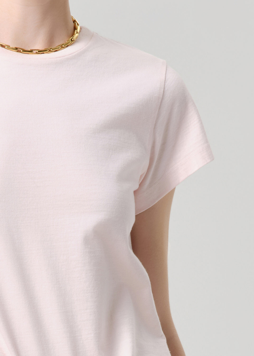 Mannequin wearing a light pink t-shirt with a gold chain necklace on a grey background