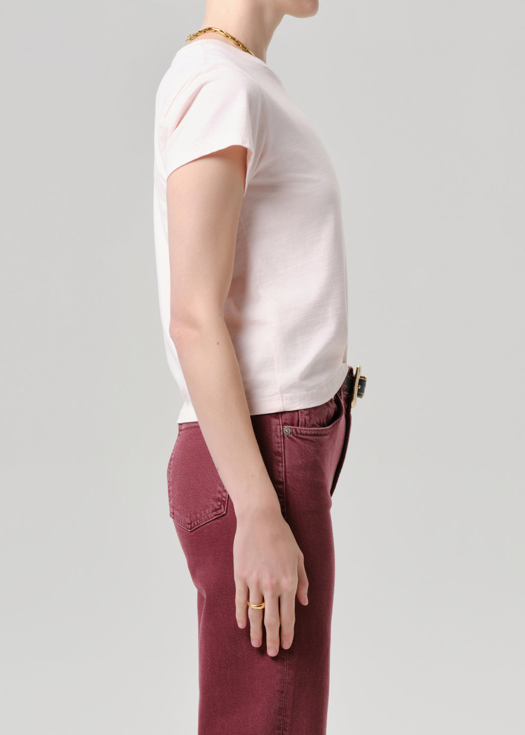 Person wearing a light pink t-shirt and maroon pants on a grey background