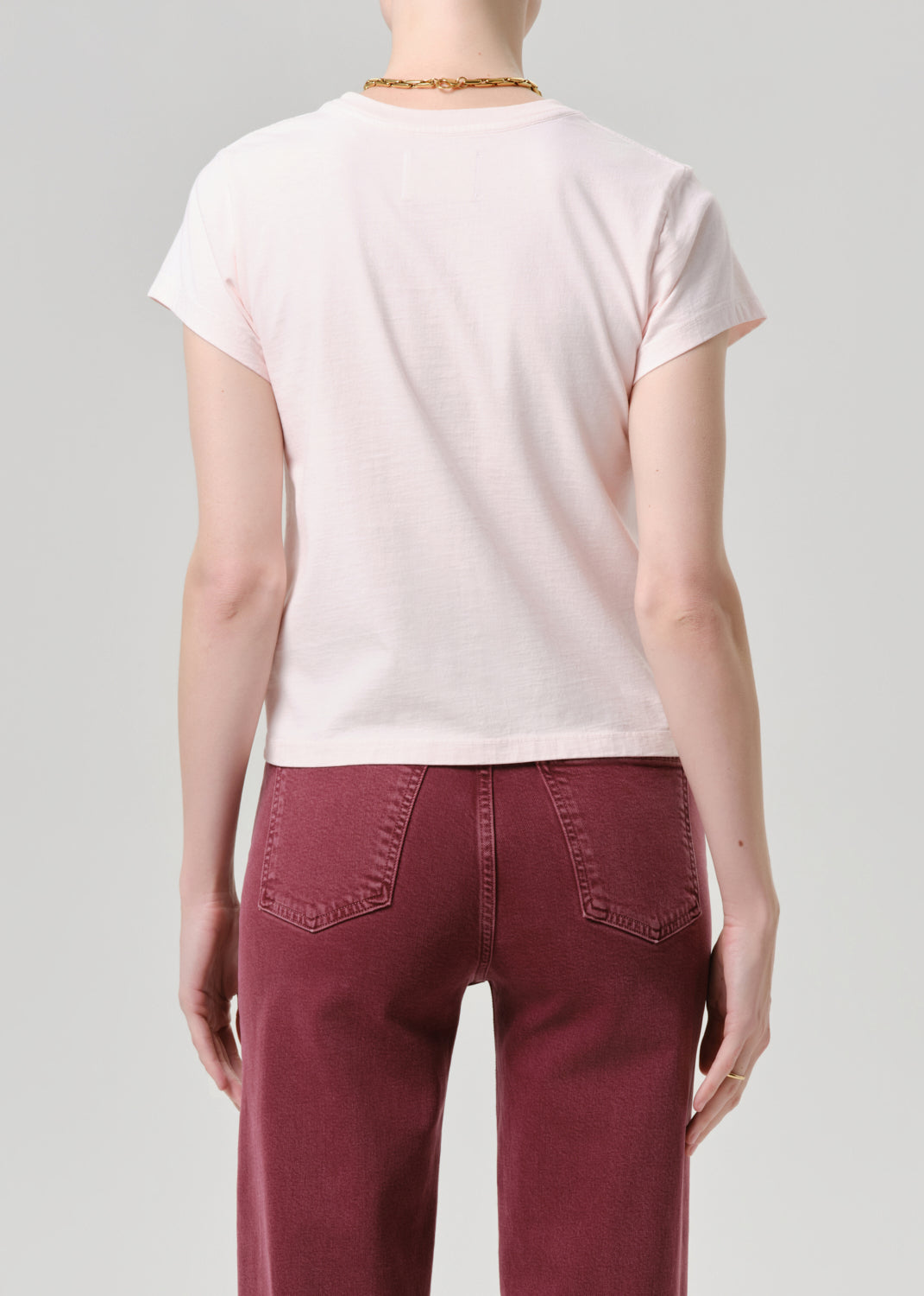 Person wearing a light pink t-shirt and burgundy pants on a grey background