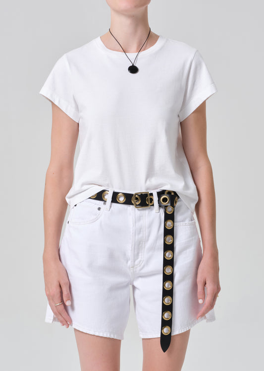 Person wearing a white t-shirt and white shorts with a decorative belt on a plain background