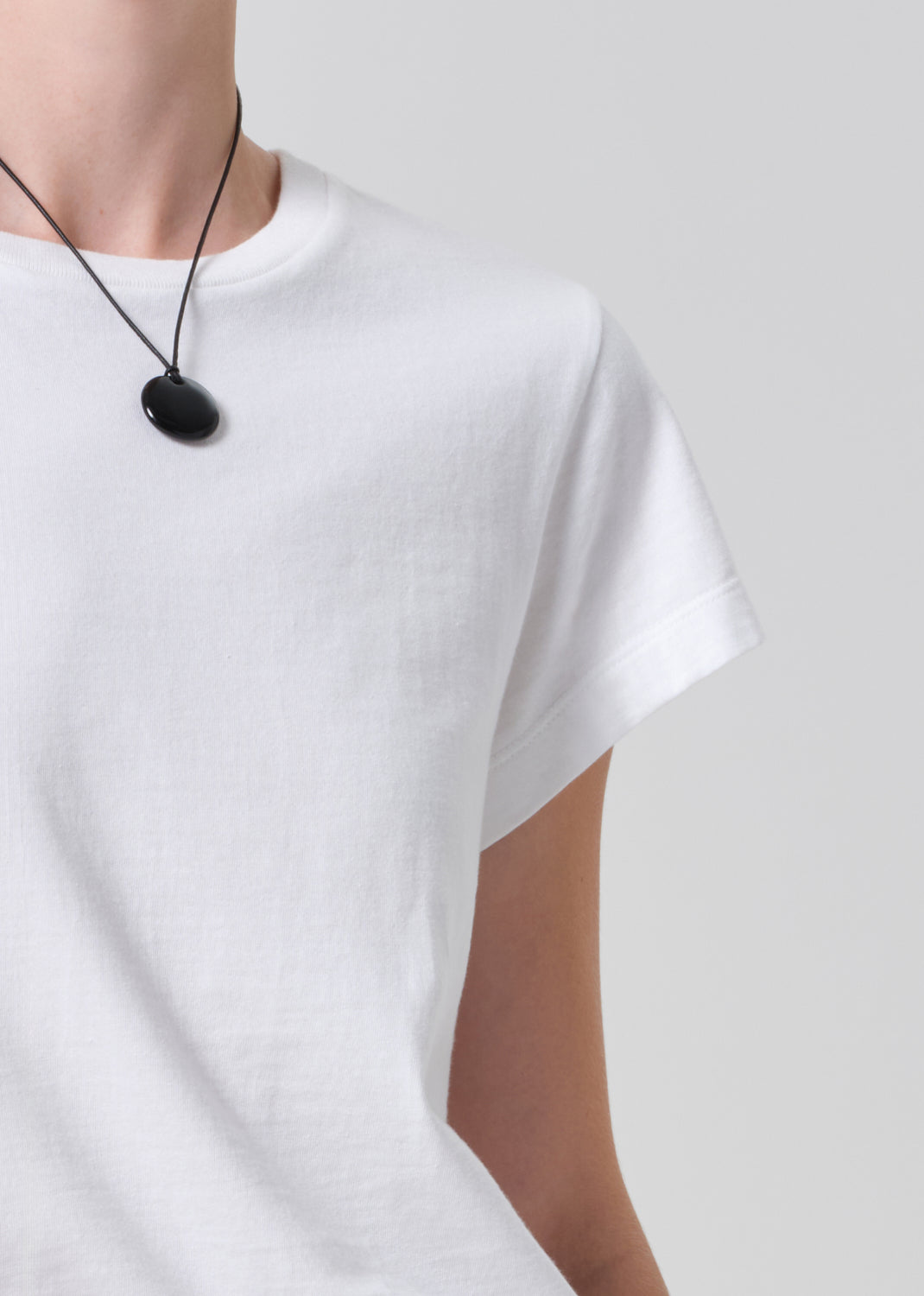 Person wearing a white t-shirt with a black necklace on a plain background