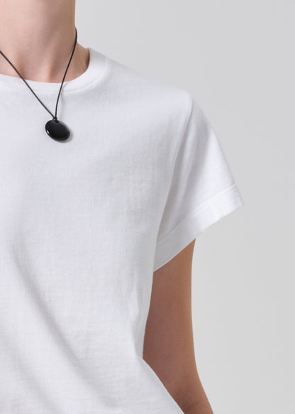 Person wearing a white t-shirt with a black necklace on a plain background