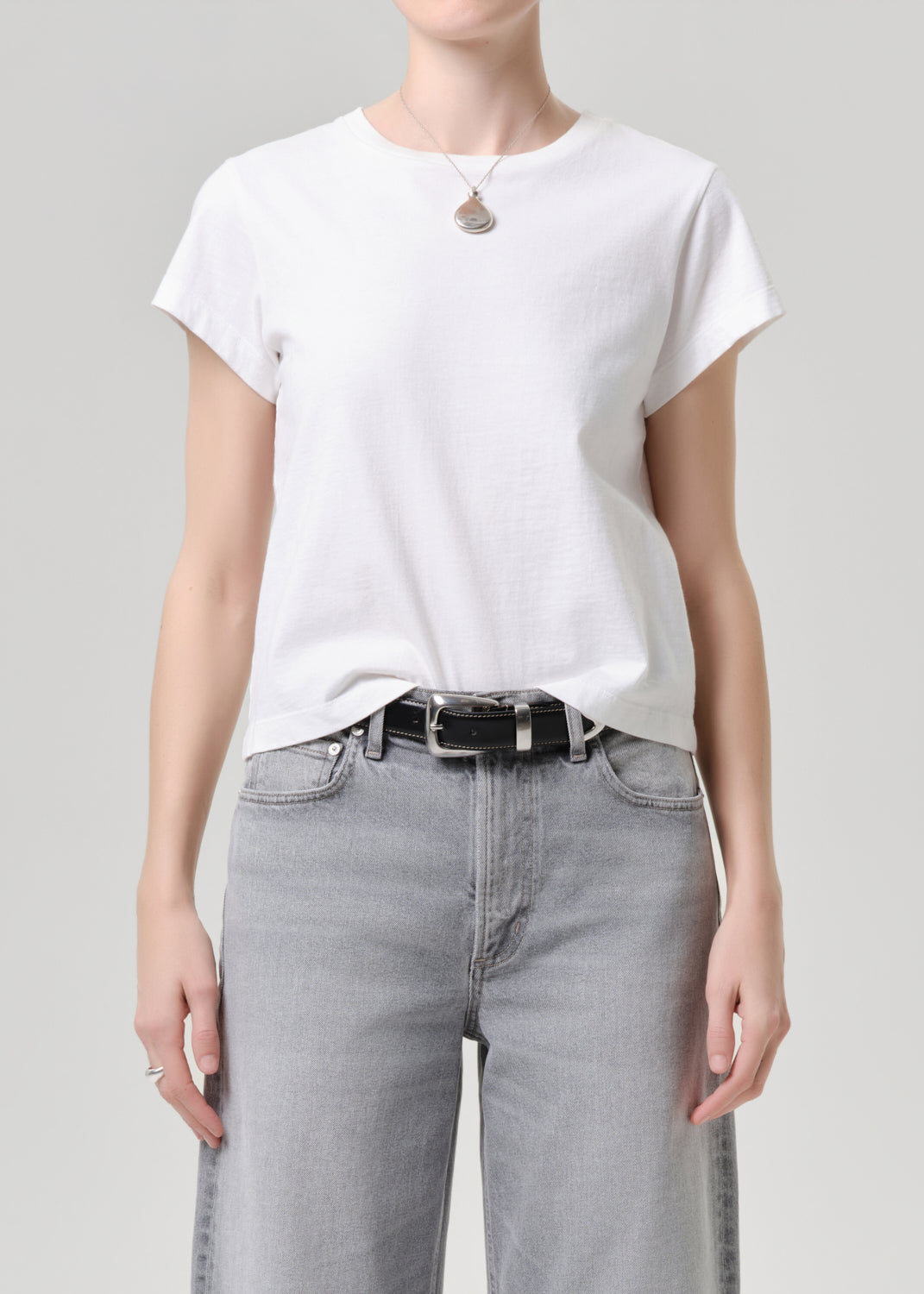 Person wearing a white t-shirt and grey jeans on a grey background.