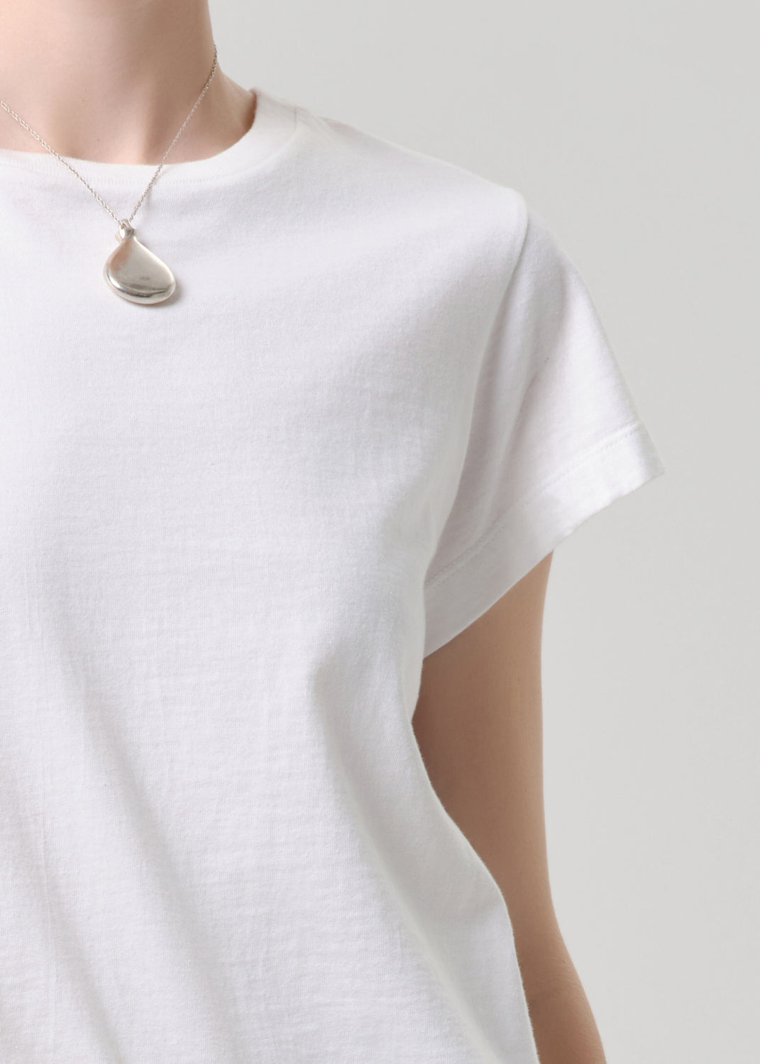 White t-shirt worn with a necklace on a grey background.