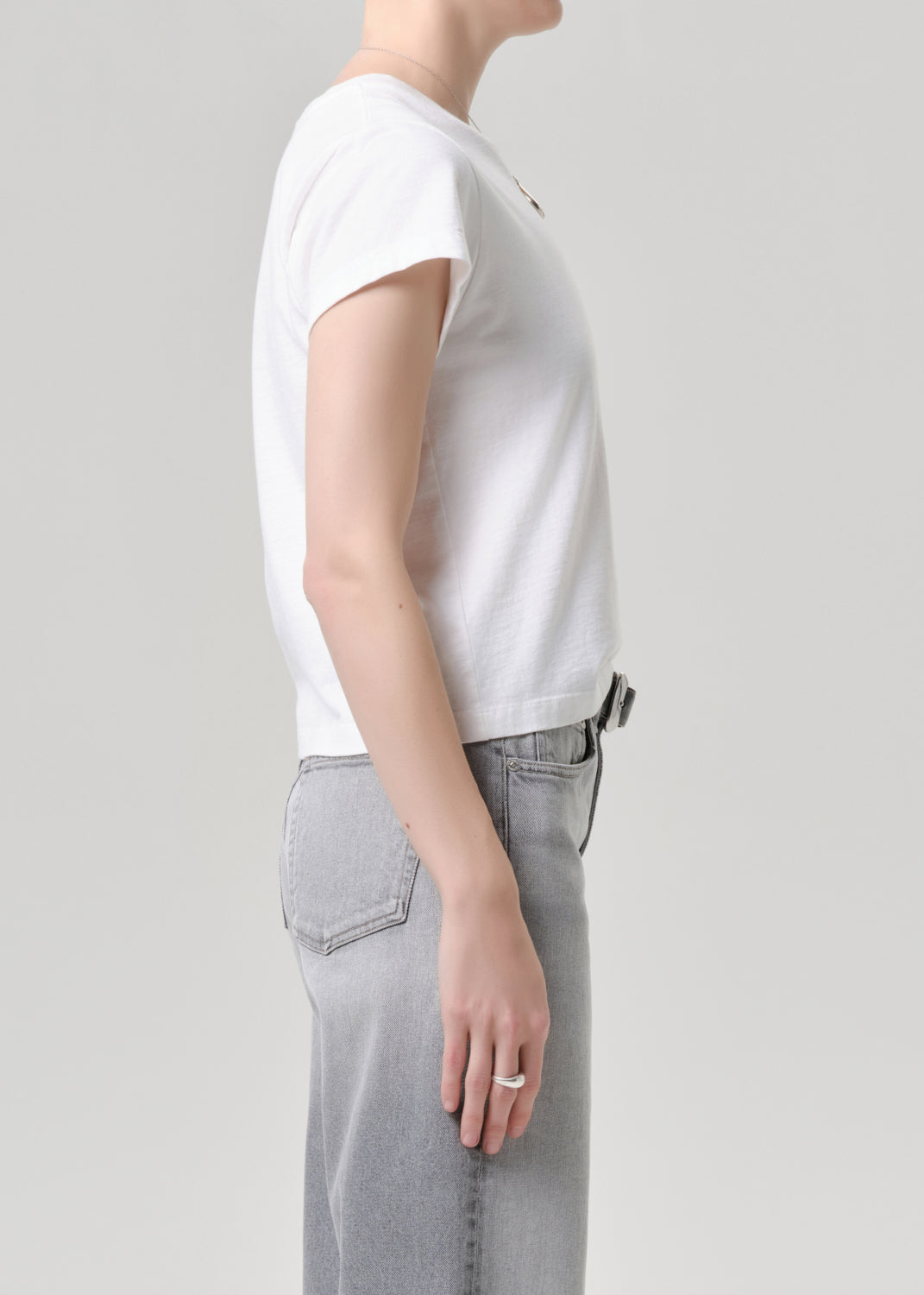 Person wearing a white t-shirt and grey pants on a grey background.