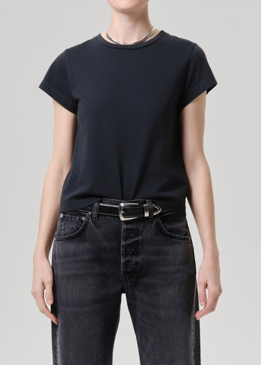 Person wearing a black t-shirt and dark jeans on a grey background.