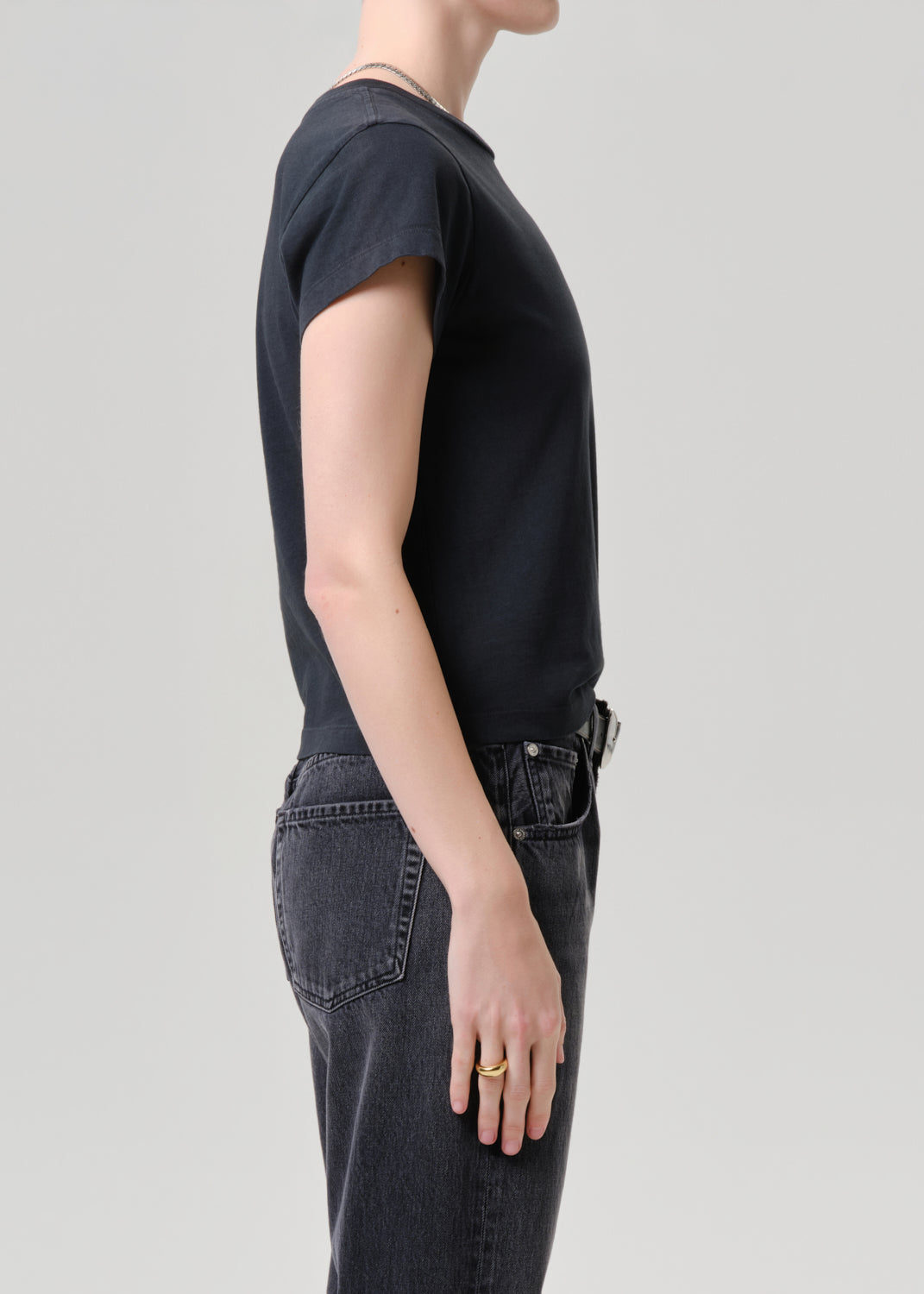 Person wearing a black t-shirt and dark jeans on a grey background.