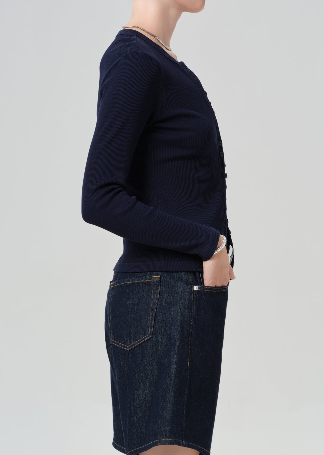 Person wearing a navy blue cardigan over dark denim shorts on a plain background