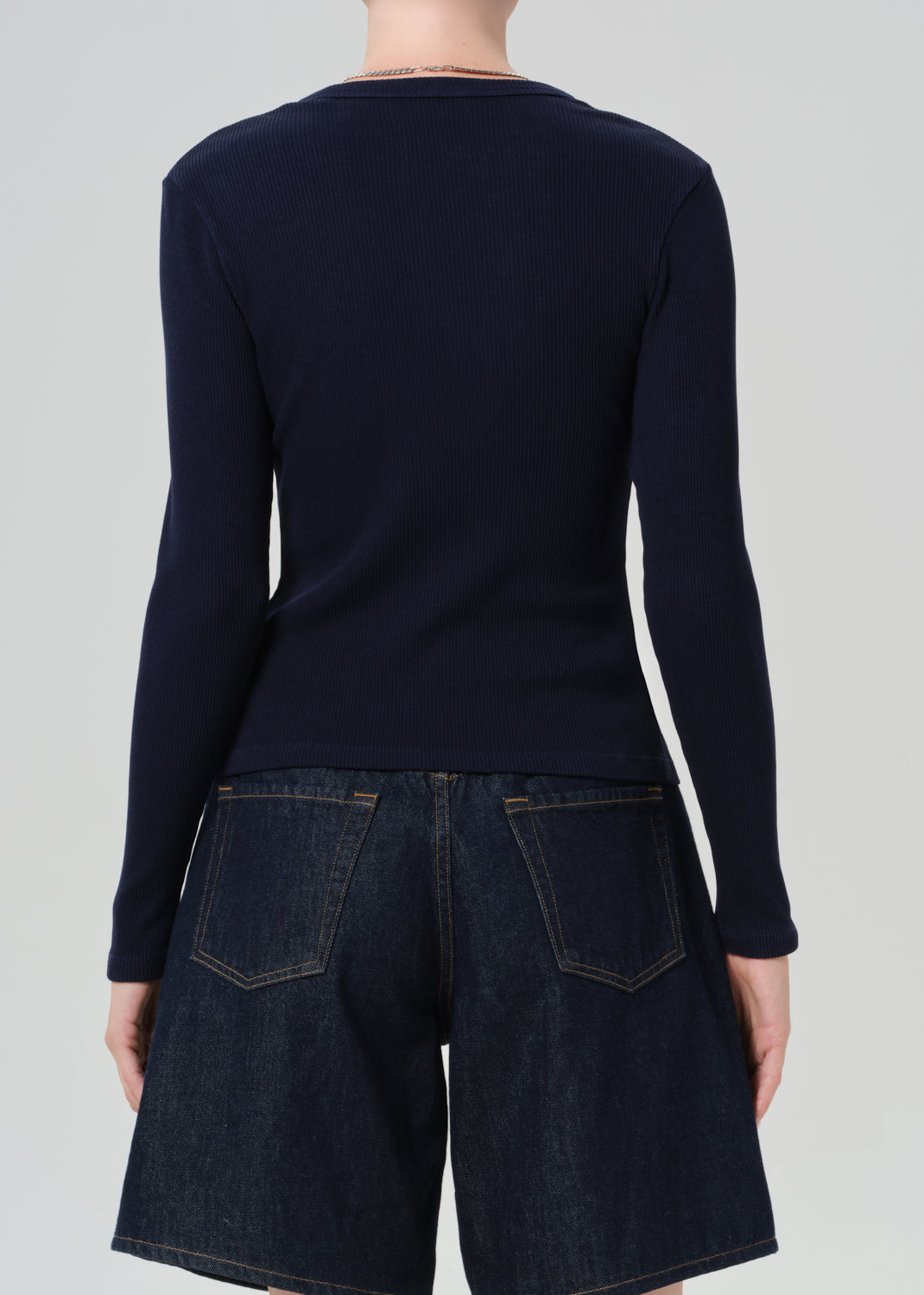 Person wearing a navy blue cardigan over dark denim shorts on a plain background