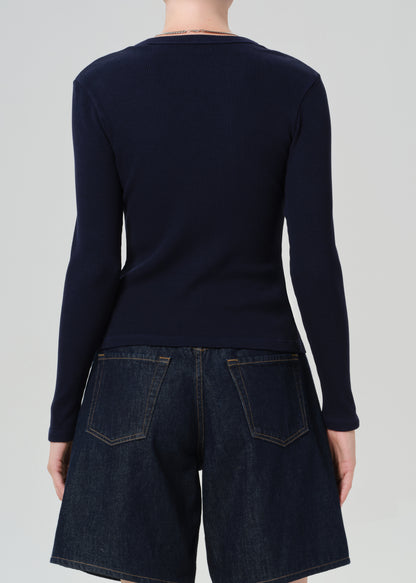 Person wearing a navy blue cardigan over dark denim shorts on a plain background