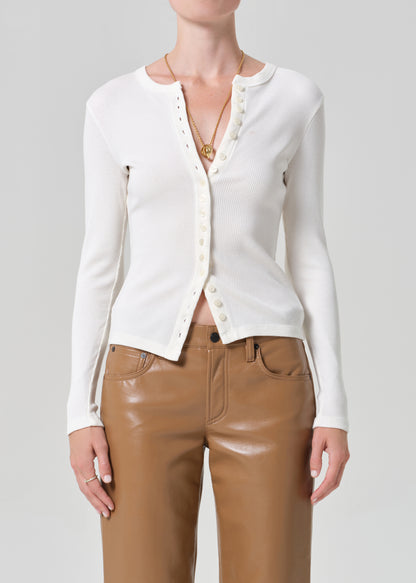 Person wearing a white cardigan and brown leather  pants on a gray background