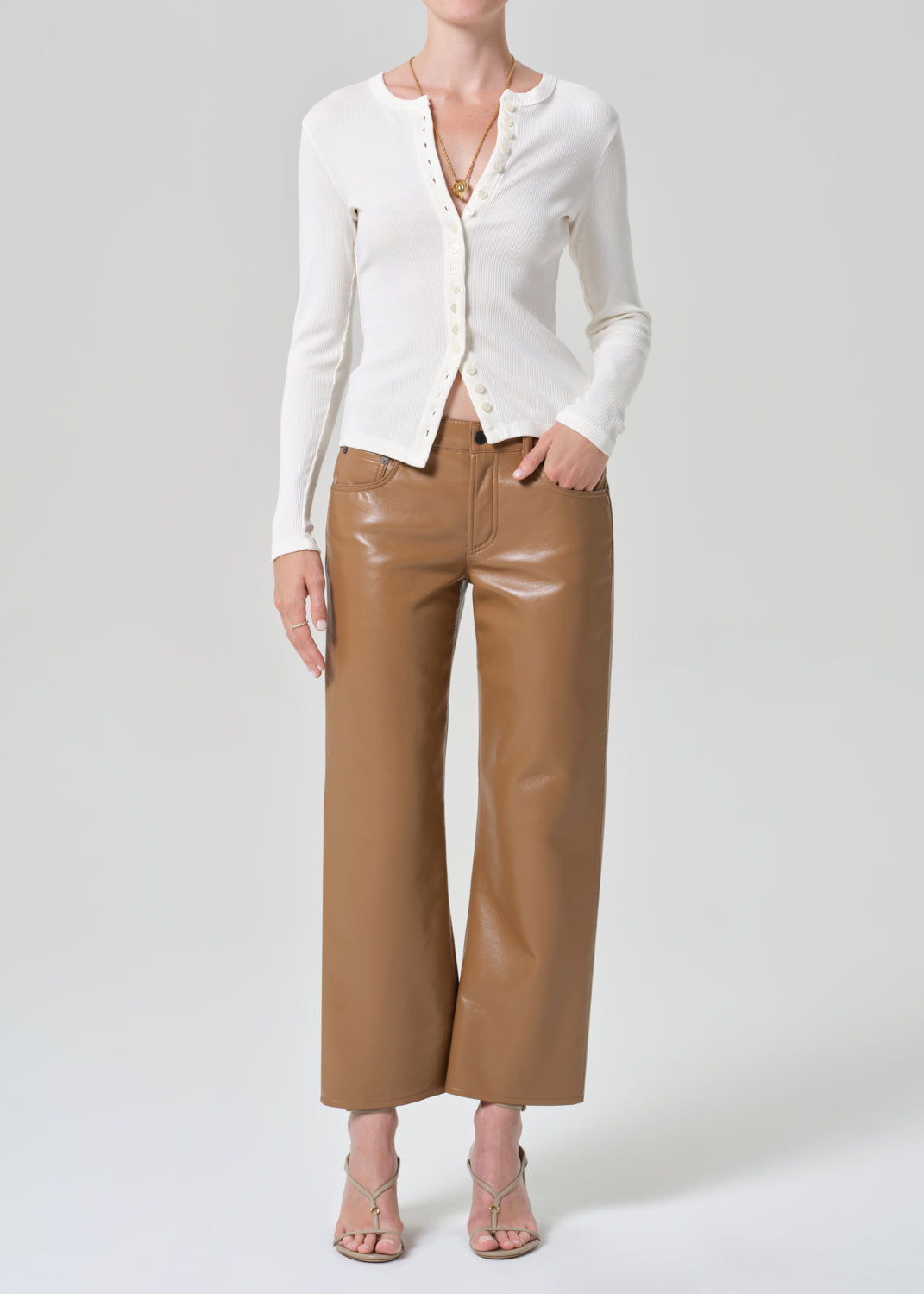 Person wearing a white cardigan and brown leather pants on a gray background