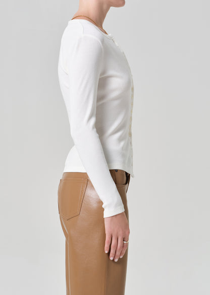 Person wearing a white cardigan and brown leather  pants on a gray background