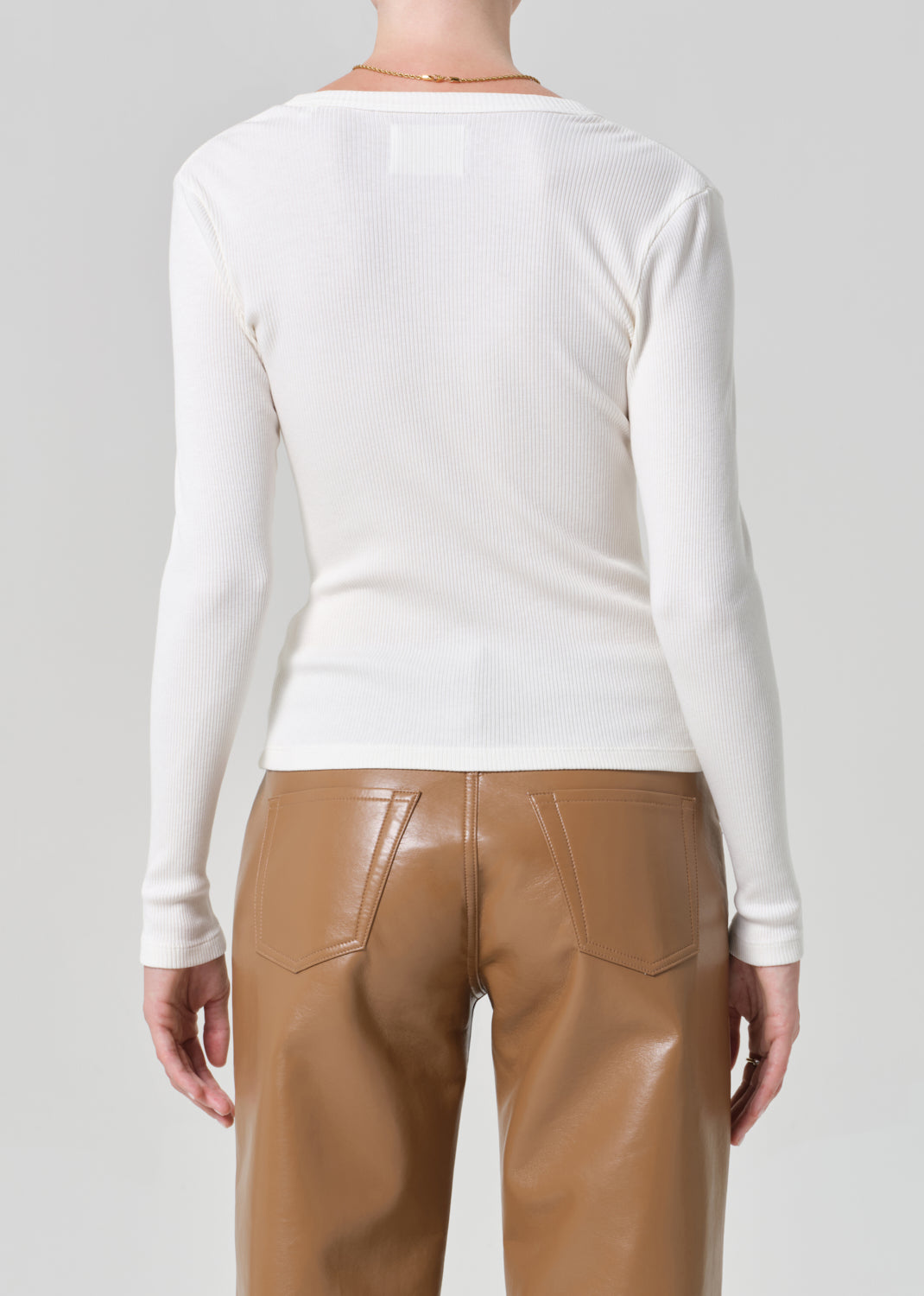 Person wearing a white cardigan and brown leather  pants on a gray background