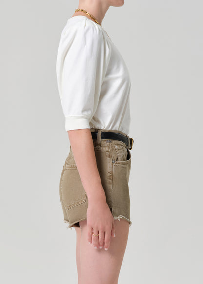 Person wearing a white blouse and beige shorts on a plain background