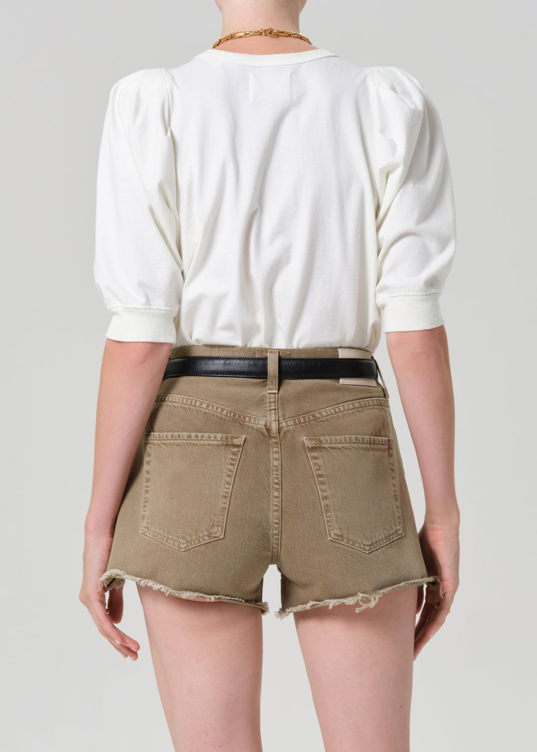 Person wearing a white blouse and khaki shorts on a plain background