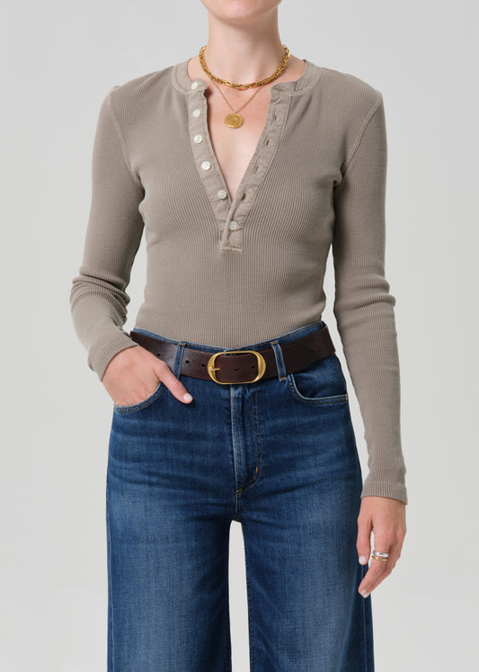 Person wearing a brown long-sleeve shirt and blue jeans on a plain background