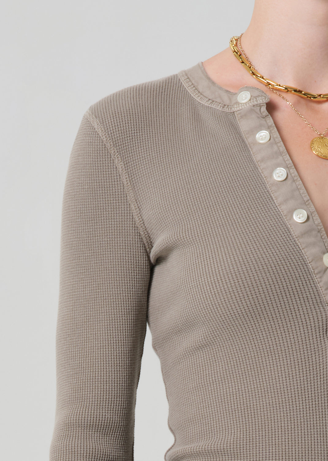 Close-up of a brown textured long-sleeve top with buttons on a light gray background