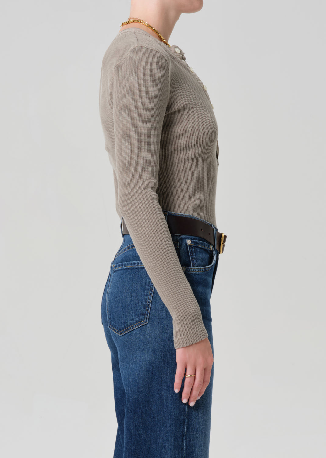 Person wearing a beige long-sleeve top and blue jeans on a plain background