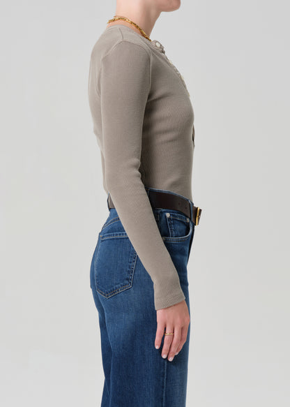 Person wearing a beige long-sleeve top and blue jeans on a plain background