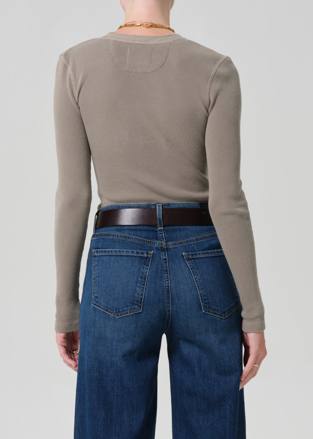 Person wearing a beige long-sleeve shirt and blue jeans on a plain background