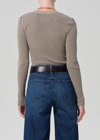 Person wearing a beige long-sleeve shirt and blue jeans on a plain background