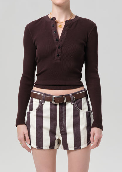 Person wearing a brown long-sleeve shirt and striped shorts on a plain background