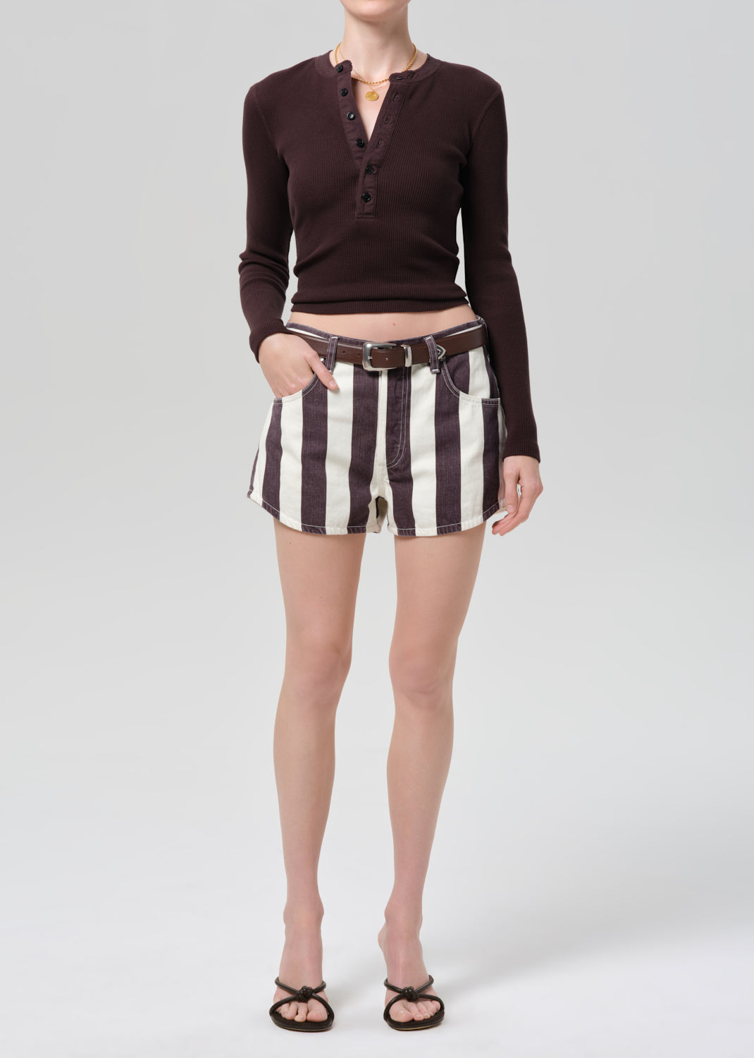 Person wearing a brown long-sleeve shirt and striped shorts on a white background