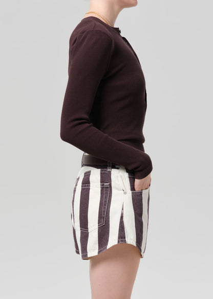 Person wearing a brown long-sleeve shirt and striped shorts on a plain background