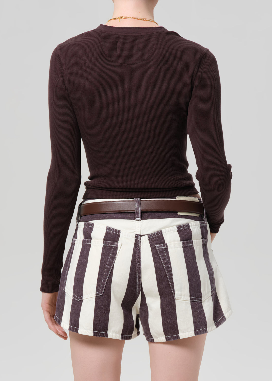 Person wearing a brown long-sleeve top and striped shorts on a plain background