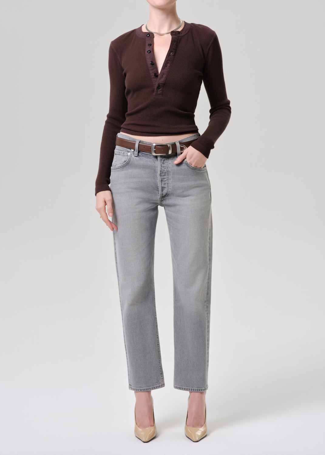 Person wearing a brown long-sleeve top and grey jeans on a grey background.