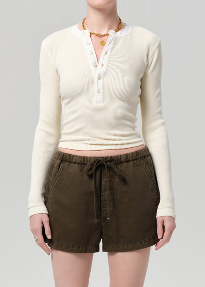 Person wearing a cream long-sleeve shirt and brown shorts on a gray background