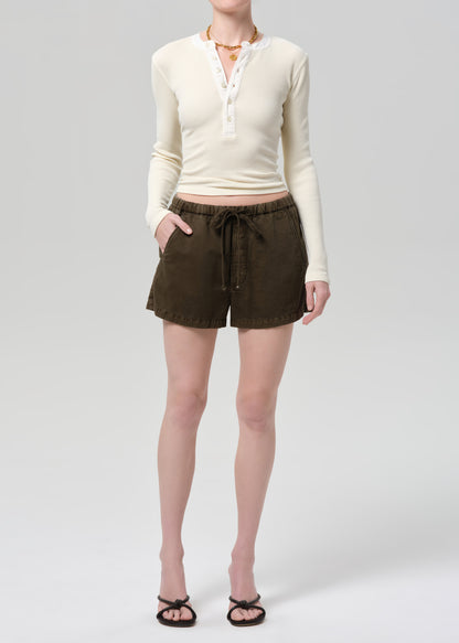 Person wearing a cream long-sleeve shirt and brown shorts on a grey background