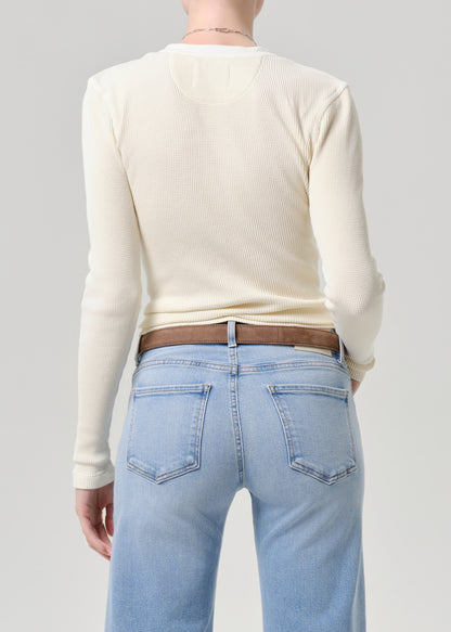 Back view of a person wearing a cream ribbed long-sleeve top, light blue jeans, and a brown belt against a grey background.