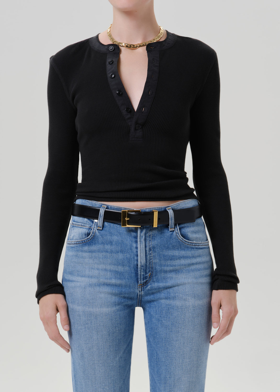 Person wearing a black long sleeve henley top with light wash straight leg jeans on a grey background
