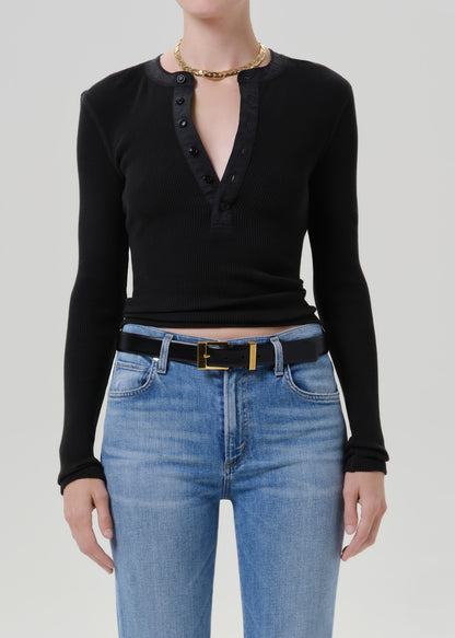 Person wearing a black long sleeve henley top with light wash straight leg jeans on a grey background