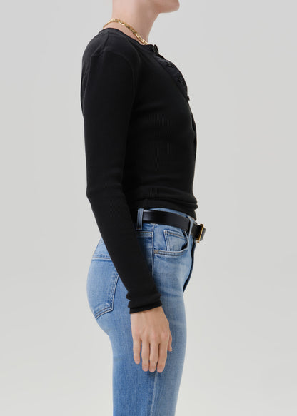 Person wearing a black long sleeve henley top with light wash straight leg jeans viewed from the side on a grey background