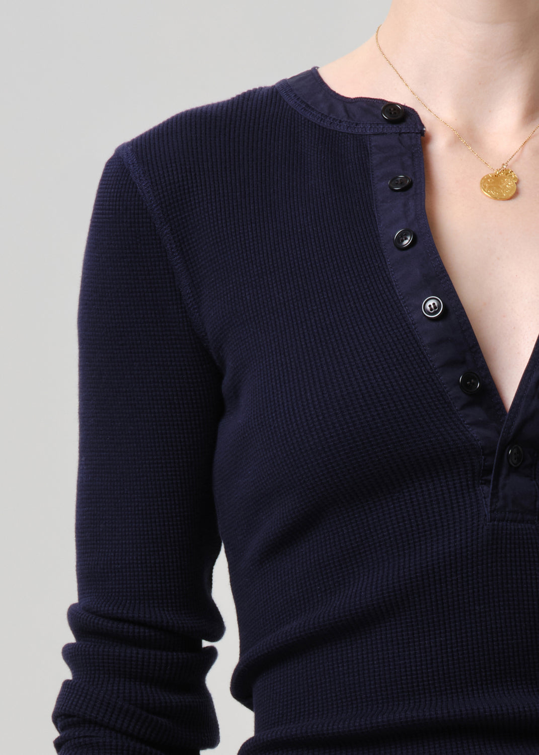 Close-up of a person wearing a dark navy ribbed long-sleeve henley top with black buttons, against a grey background.