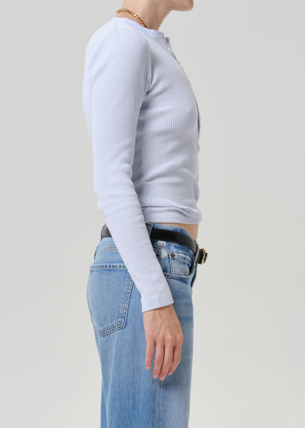 Side profile of a model wearing a light blue ribbed long-sleeve top tucked into light-wash blue jeans with a black belt.