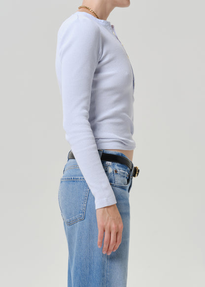 Side profile of a model wearing a light blue ribbed long-sleeve top tucked into light-wash blue jeans with a black belt.
