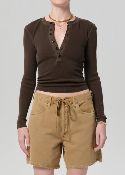 Person wearing a brown long-sleeve top and tan shorts on a plain background
