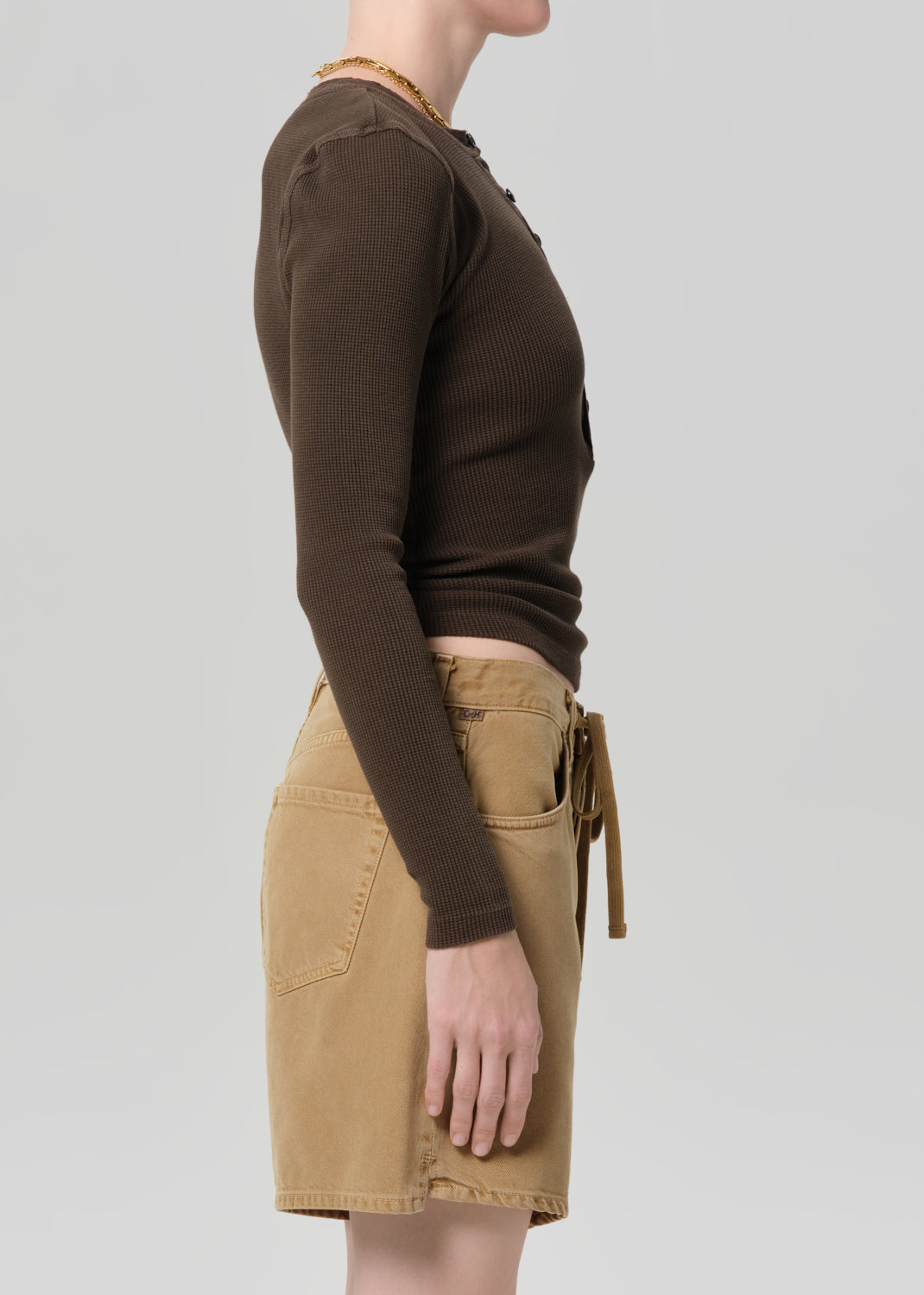 Person wearing a brown long-sleeve top and beige shorts on a light gray background