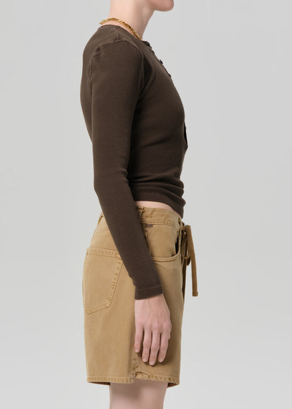 Person wearing a brown long-sleeve top and beige shorts on a light gray background