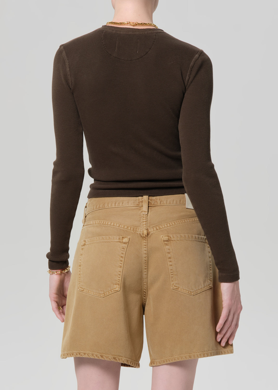 Person wearing a brown long-sleeve top and tan shorts on a plain background
