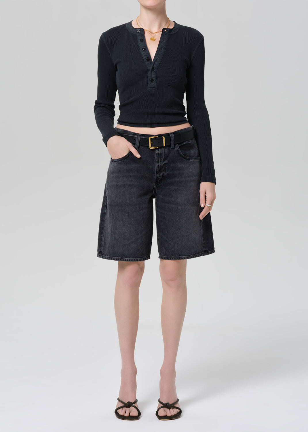 Person wearing a black long-sleeve top and black denim shorts on a plain background