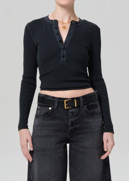 Person wearing a black long-sleeve top and black denim shorts on a plain background