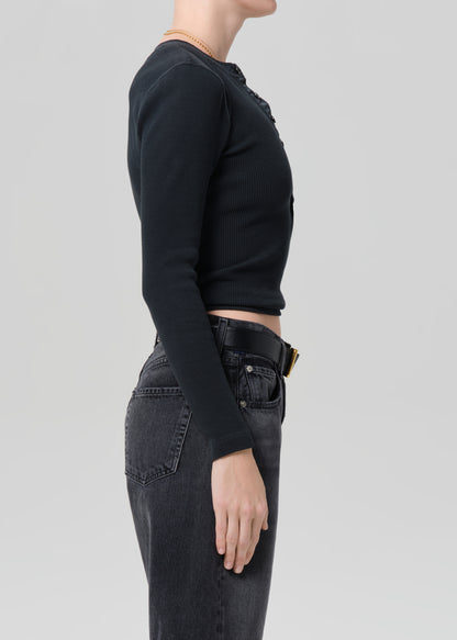 Person wearing a black long-sleeve top and black denim shorts on a plain background